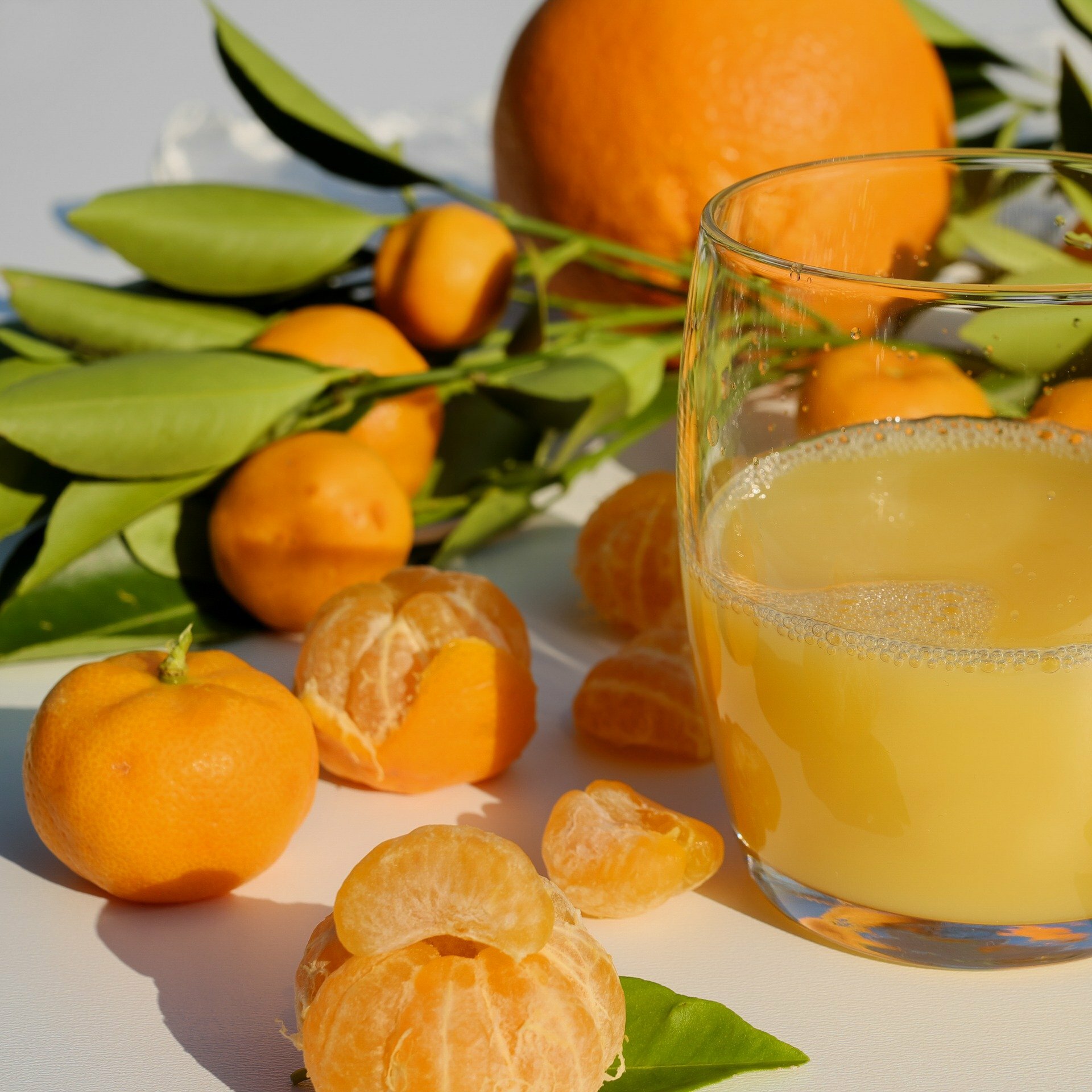 half full glass of orange juice and peeled and nonpeeled oranges on the side